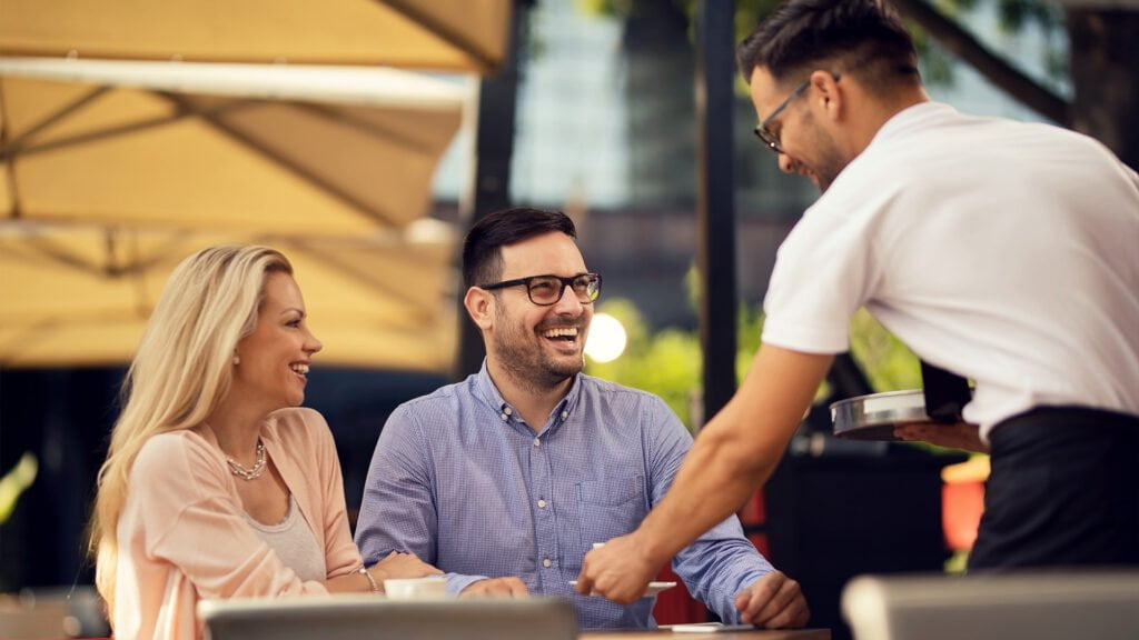 cheerful couple enjoying cafe while waiter is brining their order table 1